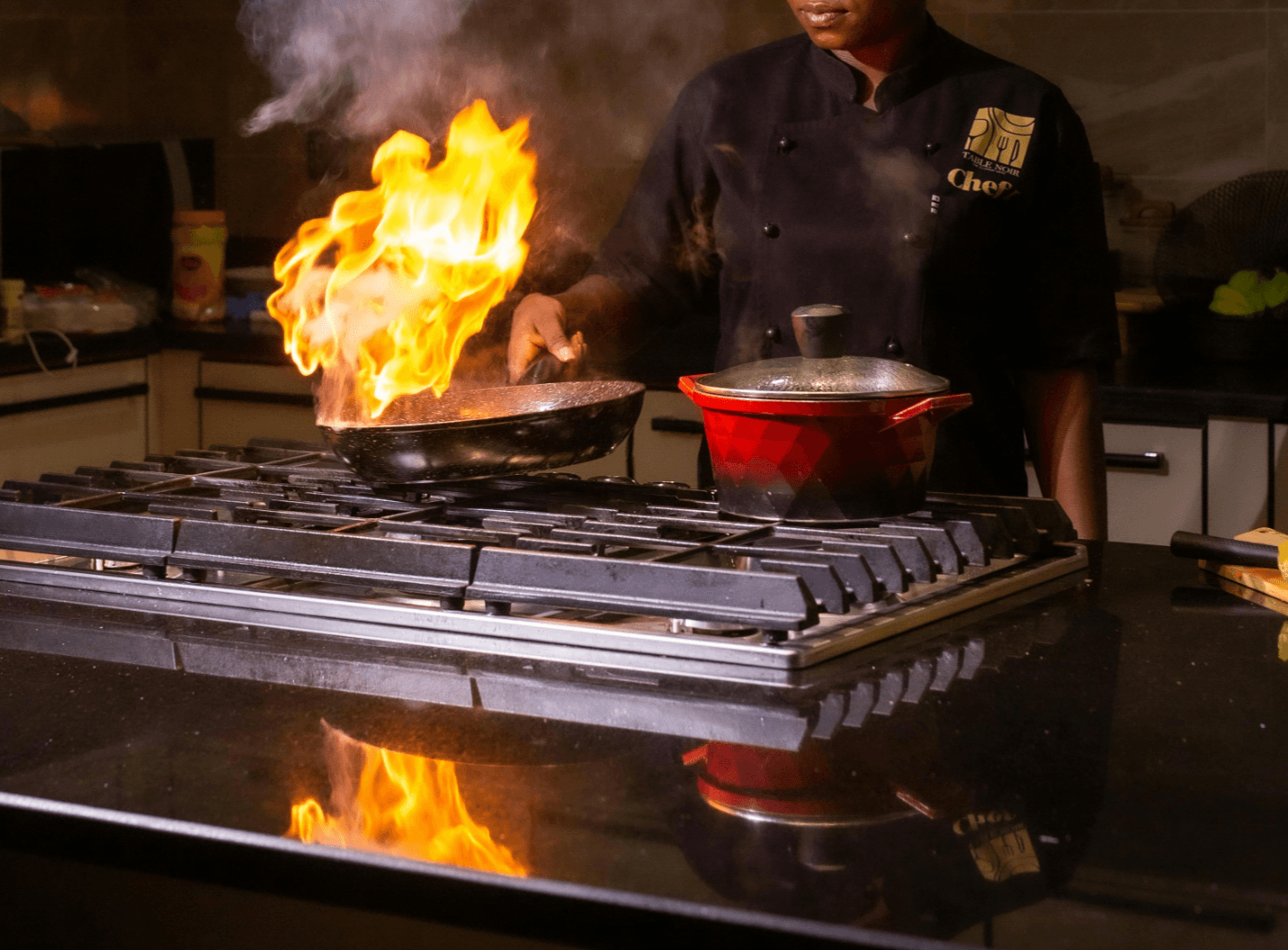 Professional chef flambéing a dish on a gas stove, flames rising from the pan in a kitchen